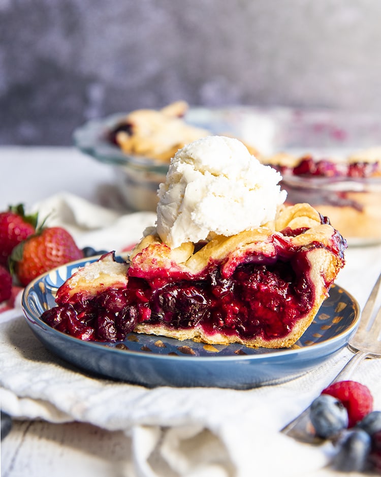 A slice of mixed berry pie on a blue plate with a scoop of vanilla ice cream on top.