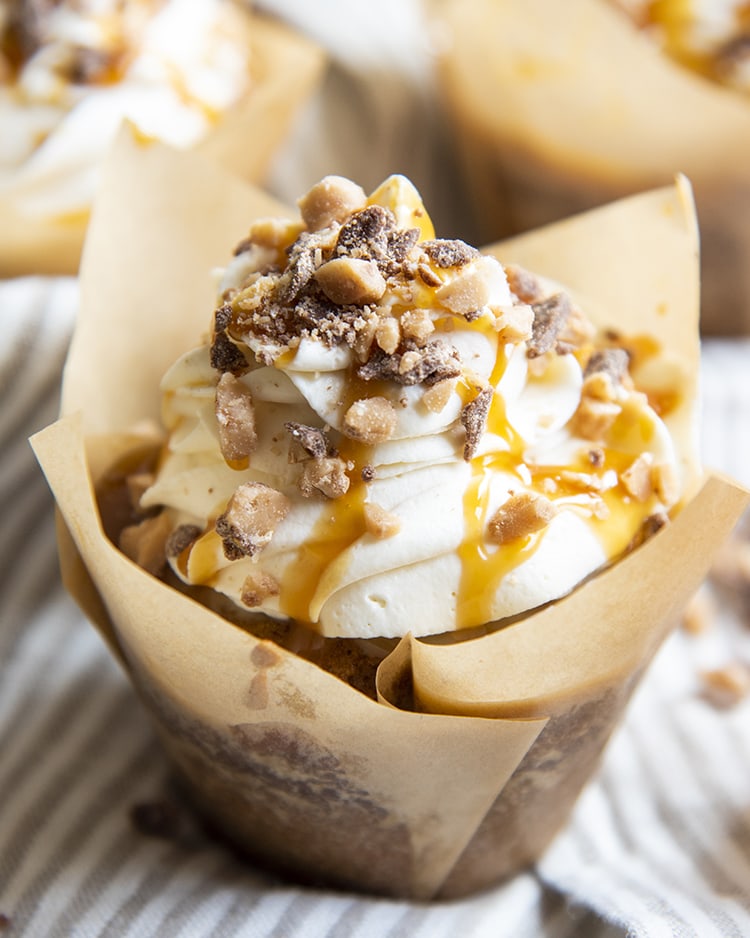 A pumpkin cupcake topped with whipped cream cheese frosting and toffee bits in a tulip shaped cupcake wrapper.