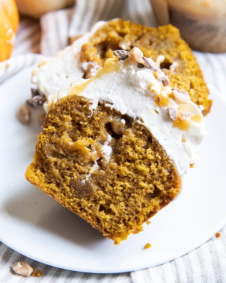 A pumpkin cupcake cut in half showing the moist middle of the pumpkin, topped with frosting.