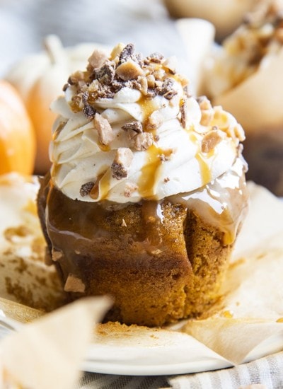 A pumpkin better than sex cupcake with caramel dripping down the sides, topped with cream cheese frosting, and a a caramel drizzle, and toffee bits.