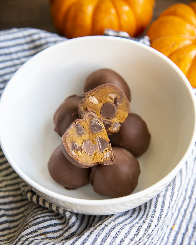 Pumpkin Cookie Dough Truffles displayed in a bowl with one cut in half to reveal the filling.