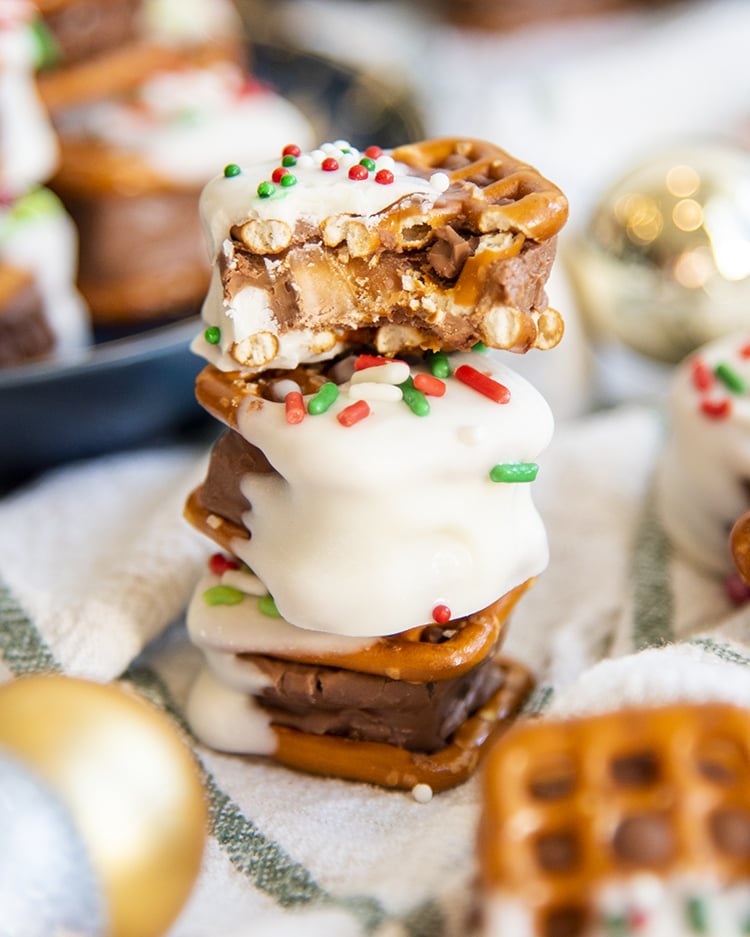 Candy bar pretzel bites in a stack, and the top one has a bite taken out of it showing the caramel middle.