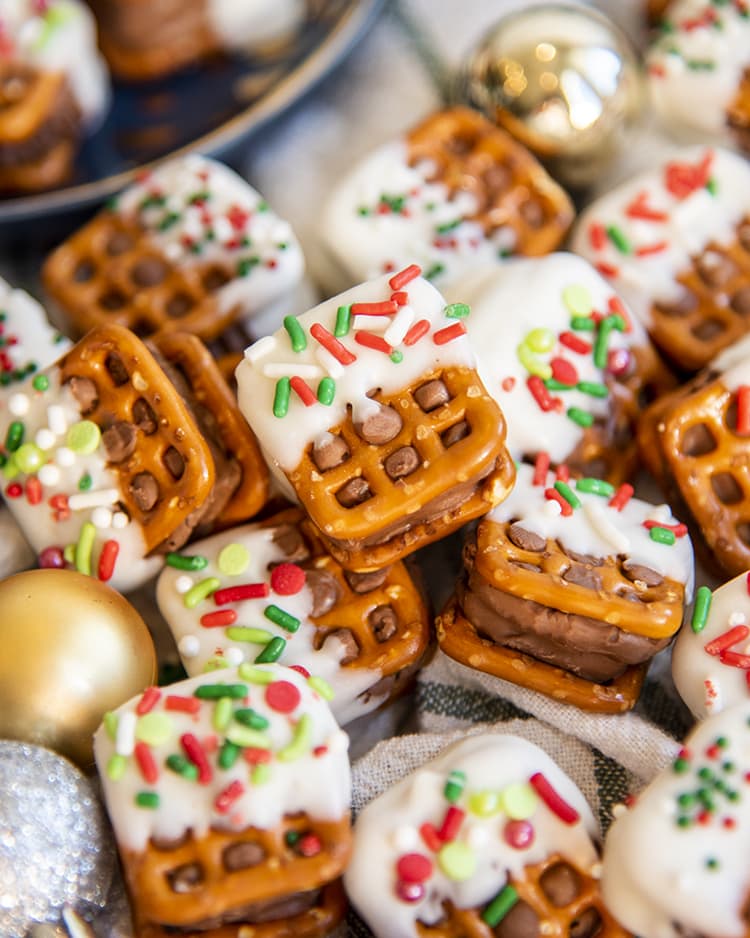A pile of candy bar pretzel bites, that are dipped half in white chocolate and christmas sprinkles.