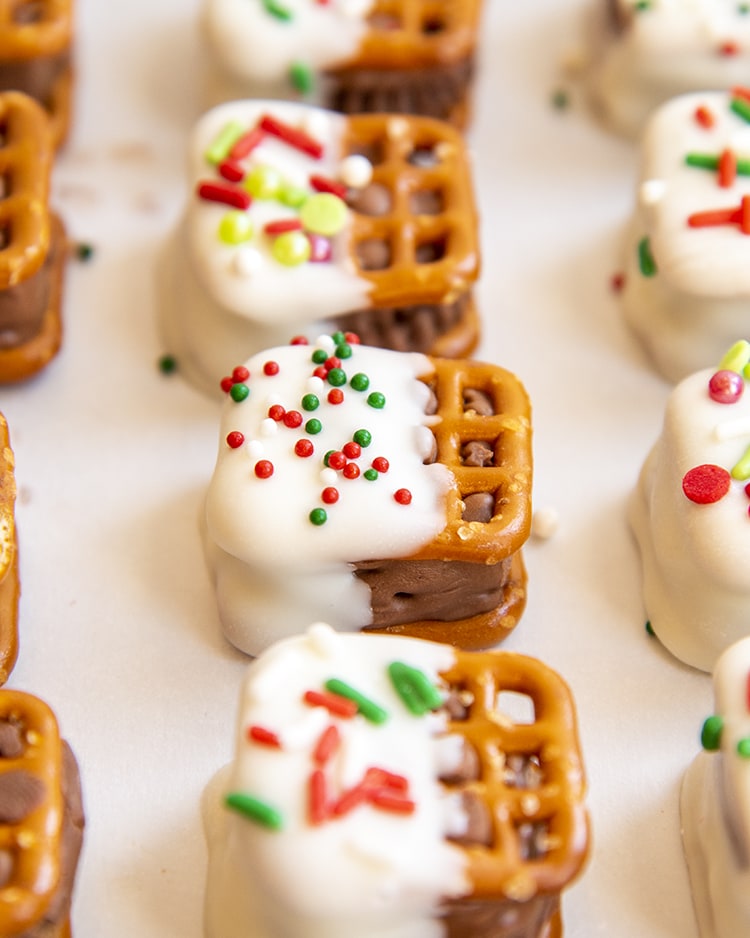 A row of candy bar pretzel bites that are dipped in white chocolate, and topped with Christmas sprinkles.