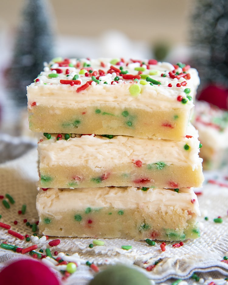 A stack of sugar cookie bars filled with red and green jimmie sprinkles, and topped with a white frosting, and more sprinkles.