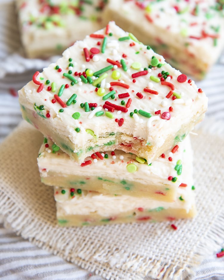 A stack of sugar cookie bars filled with red and green jimmie sprinkles, and topped with a white frosting, and more sprinkles.