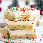 A stack of sugar cookie bars with red and green jimmie sprinkles, and topped with a white frosting
