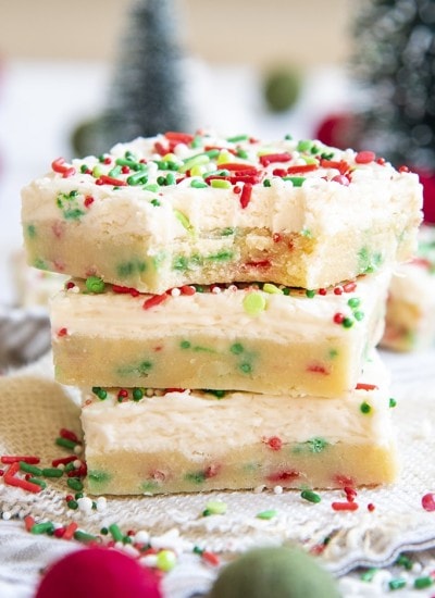 A stack of sugar cookie bars with red and green jimmie sprinkles, and topped with a white frosting