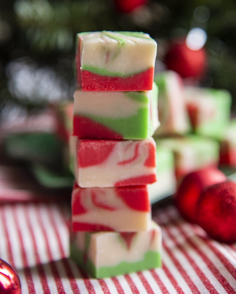 A stack of 5 pieces of fudge, swirled with red, and green and white throughout the pieces.