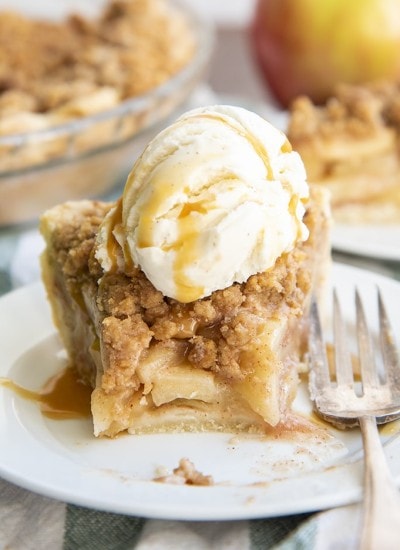 A slice of dutch apple pie with a bite out of it, then topped with ice cream, all on a plate.
