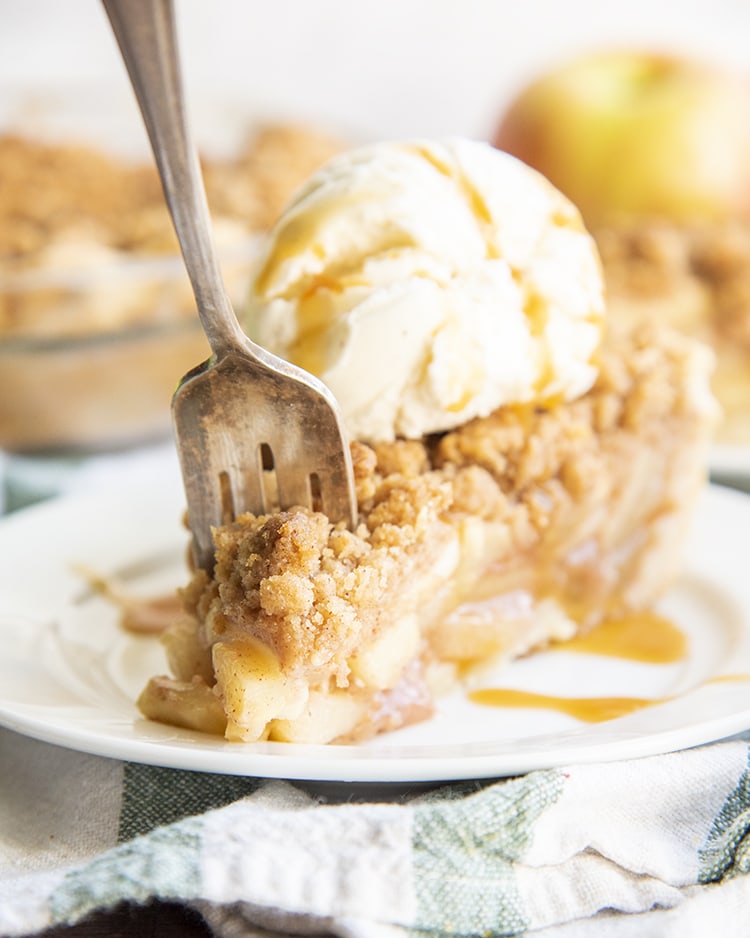 A slice of apple pie on a plate with ice cream and caramel on top.