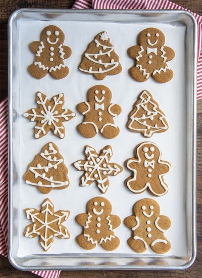 A cookie sheet lined with gingerbread cookies. There are gingerbread men, trees, and snowflakes, decorated with a simple royal icing.