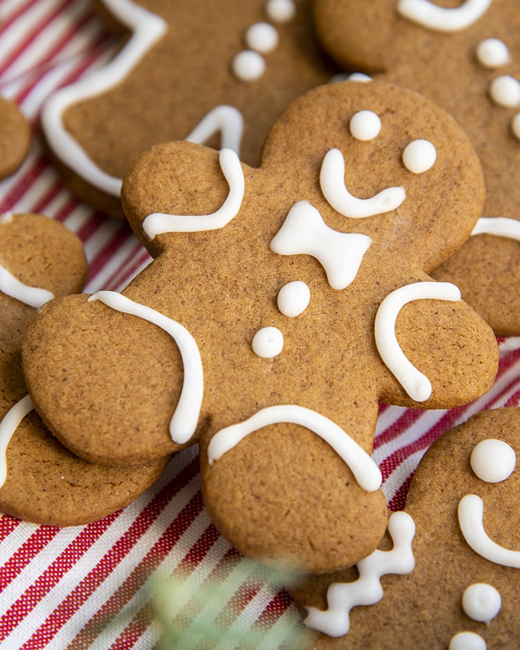 A pile of gingerbread men cookies. The top cookie is decorated with a little white icing bow tie, two buttons, and a smiling face.