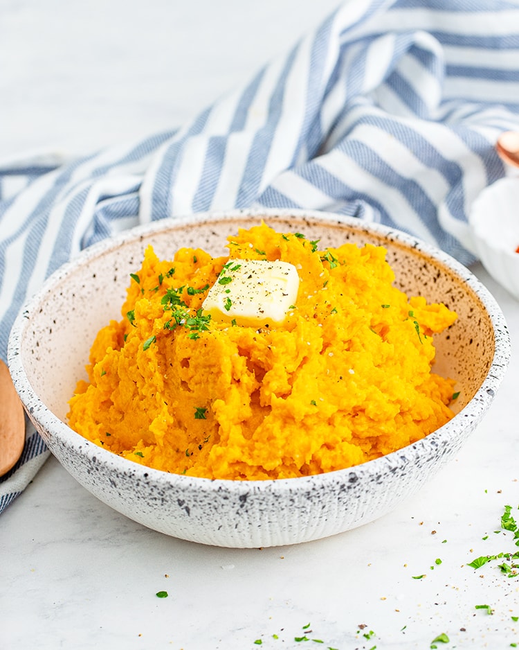 A bowl of mashed sweet potatoes topped with a pat of butter and sprinkled with parsley.