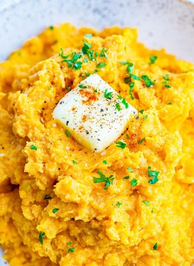 A close up of mashed sweet potatoes, topped with a pat of butter, sprinkled with parsley and chipotle powder.