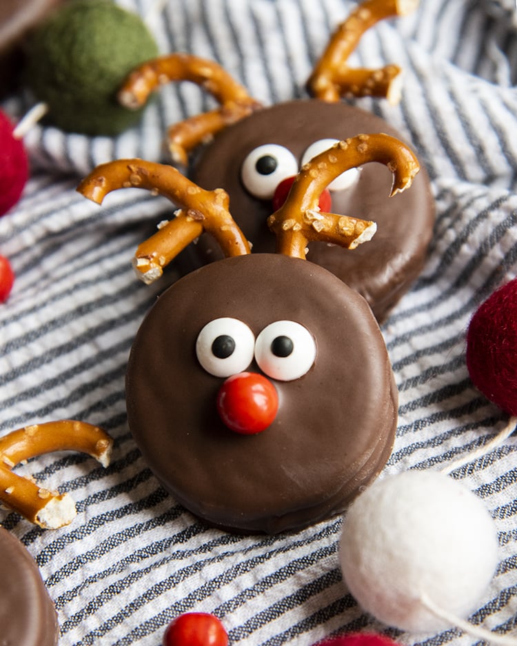 Two Oreos decorated with chocolate, candy eyes, and pretzels to look like reindeer.