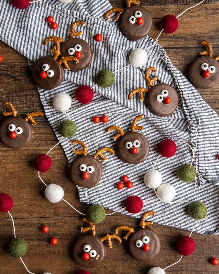 Oreos decorated like reindeer and scattered over a blue and white striped cloth.