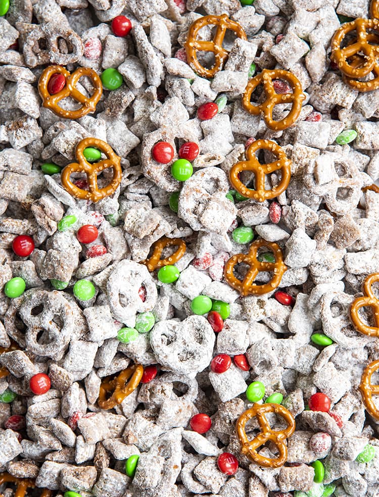 Christmas Muddy Buddies on a baking sheet lined with parchment paper. There are muddy buddies, red and green m&ms, and mini pretzels.