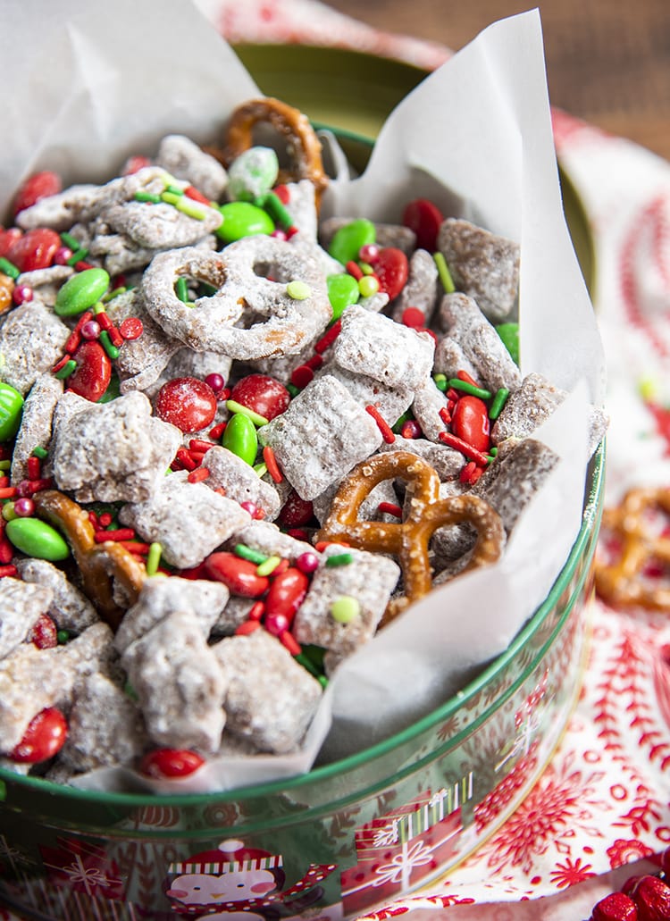 A close up of a Christmas tin full of Reindeer chow which is muddy buddies with red and green m&ms, and mini pretzels.