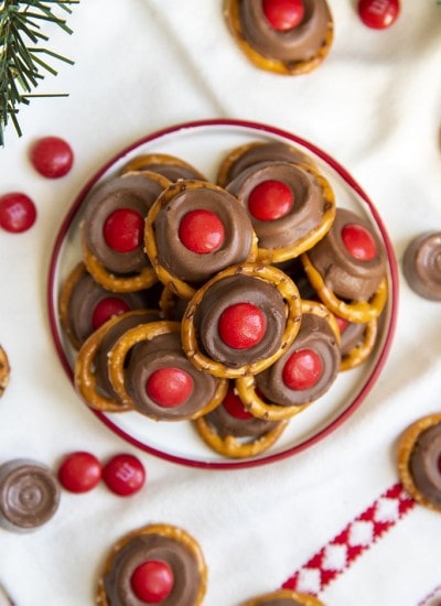 A small plate full of "rudolph noses" treats. Which are round pretzels topped with a slightly melted rolo, and a red m&m on top.