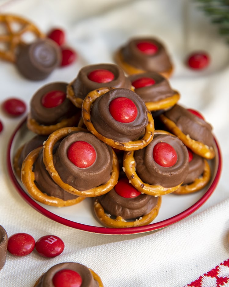 A small plate full of "rudolph noses" treats. Which are round pretzels topped with a slightly melted rolo, and a red m&m on top.