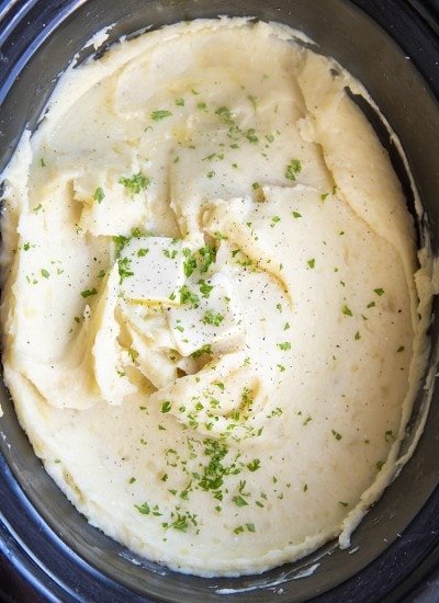Mashed Potatoes in a slow cooker topped with butter and sprinkled parsley.