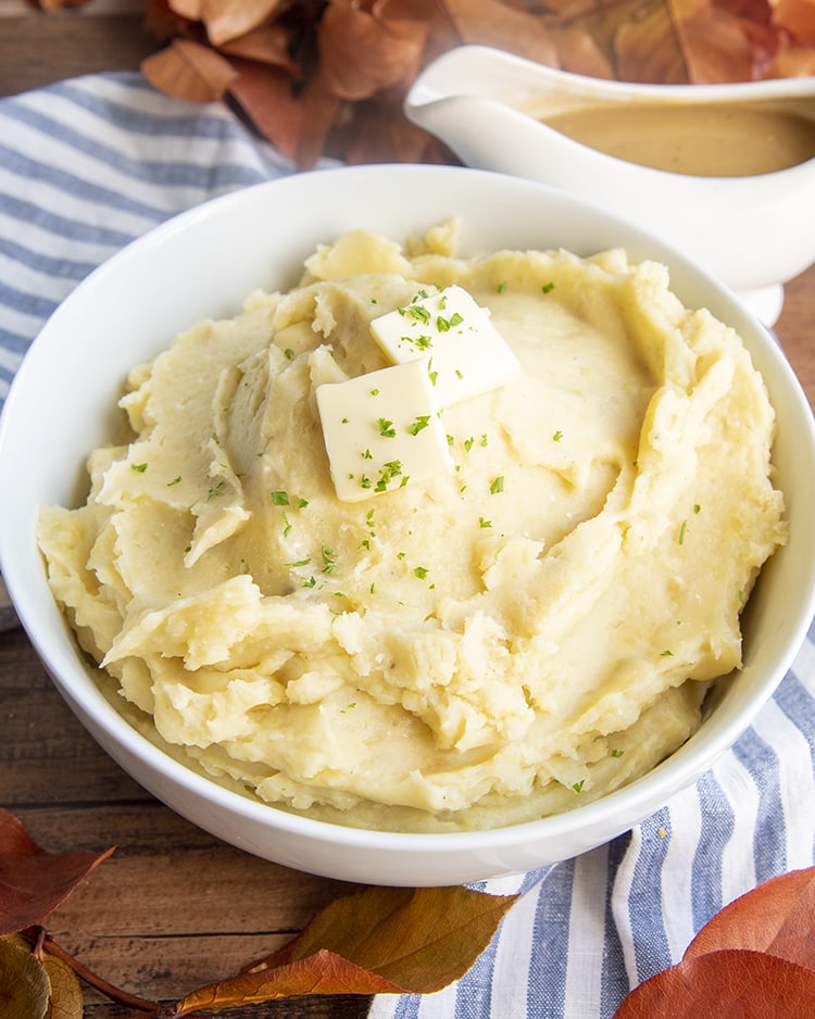 A big bowl of slow cooker mashed potatoes topped with butter and sprinkled with parsley.