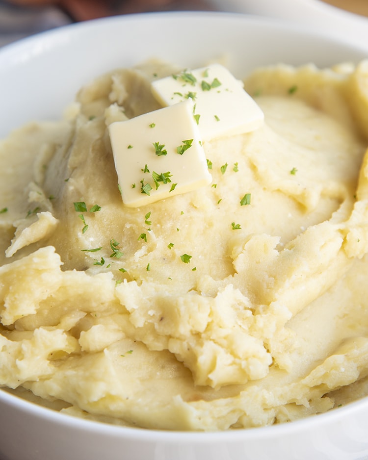 A big bowl of slow cooker mashed potatoes topped with butter and sprinkled with parsley.