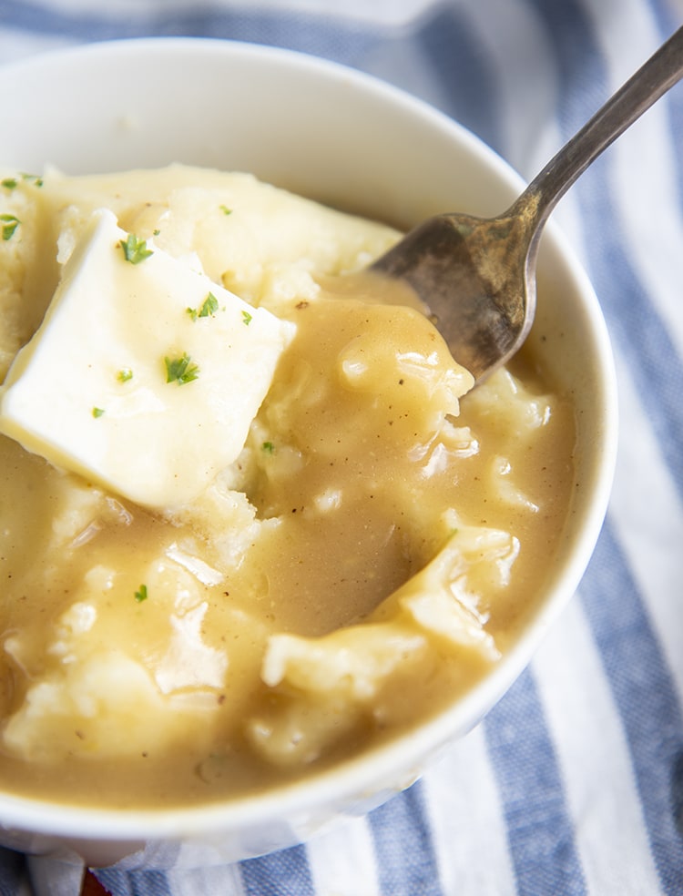A bowl of mashed potatoes topped with a pat of butter, and turkey gravy.
