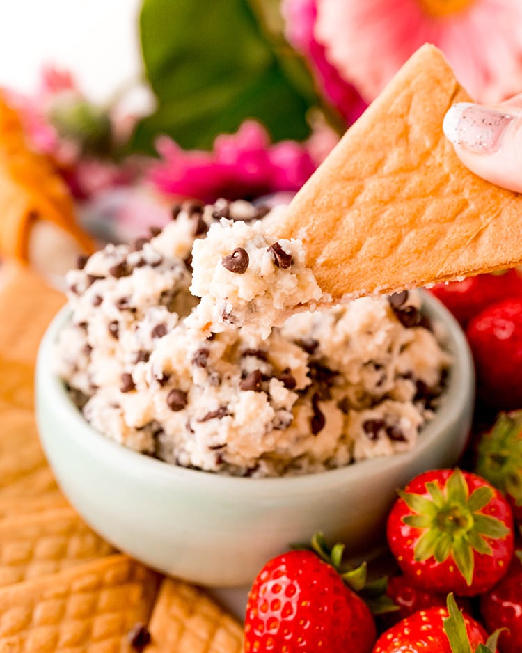 A bowl of cannoli dip sprinkled with mini chocolate chips, with a triangle shaped crepe cookie lifting some of the dip out of the bowl.