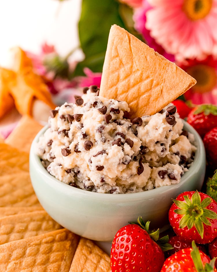 A bowl of cannoli dip sprinkled with mini chocolate chips, with a triangle shaped crepe cookie sticking in the dip.