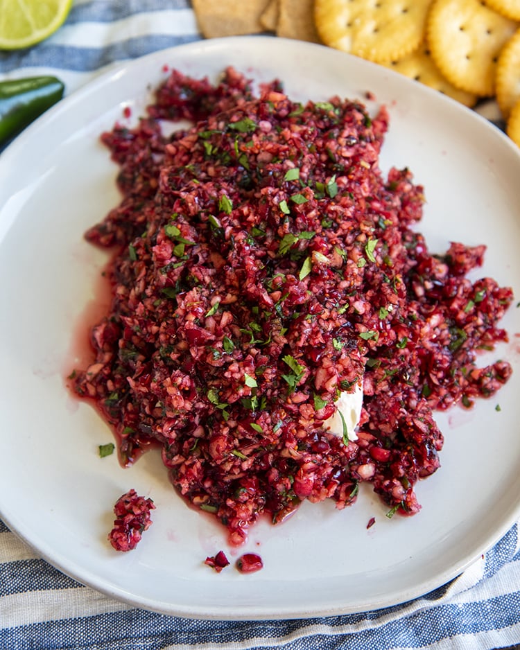 Cranberry salsa over a cream cheese block on a white plate. The cream cheese is barely showing through the salsa in one corner.