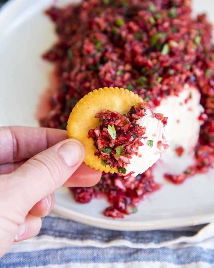 Cranberry salsa and cream cheese on a ritz cracker in front of a plate of cranberry salsa over a block of cream cheese.