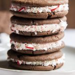 A stack of homemade cake mix oreo cookies with peppermint candy cane pieces stuck to the frosting in the middle.