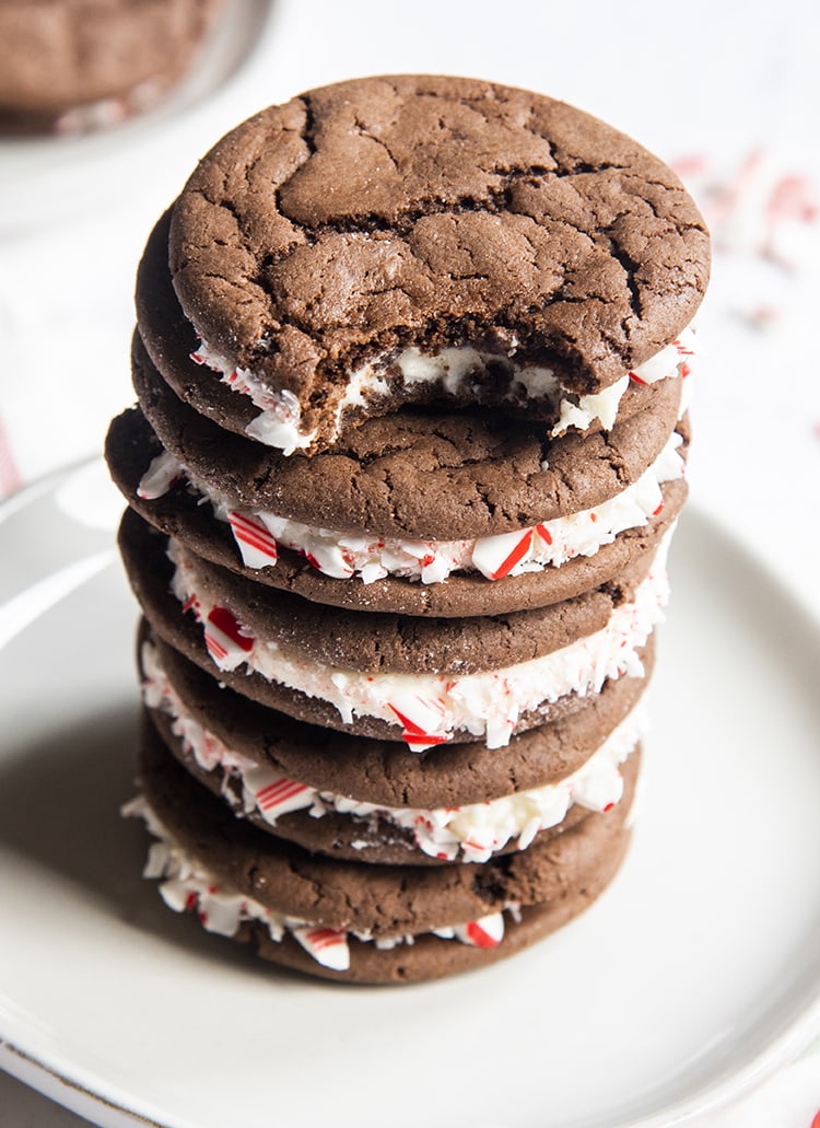A stack of homemade cake mix oreo cookies with peppermint candy cane pieces stuck to the frosting in the middle. The top cookie on the stack has a bite out of it.