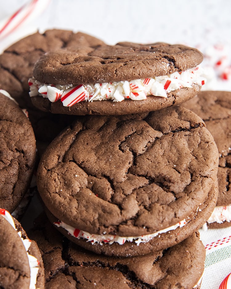 A pile of cake mix cookie sandwiches, filled with white frosting and the frosting is coated in candy cane pieces.