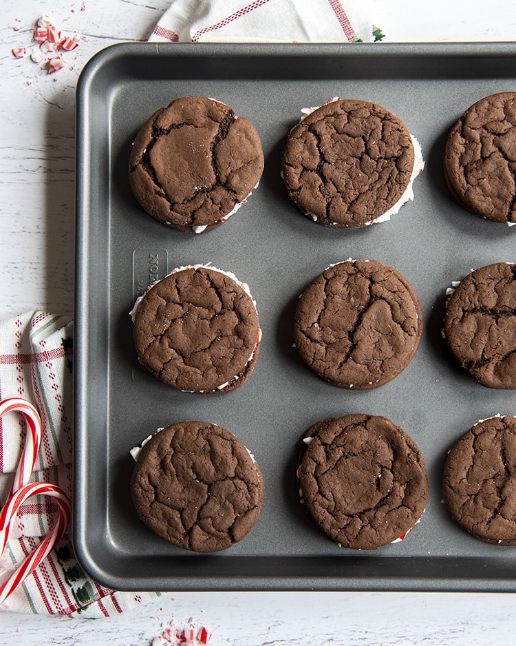 Nine cake mix homemade oreo cookies on a baking pan, some of the white frosting is showing sticking out the sides.