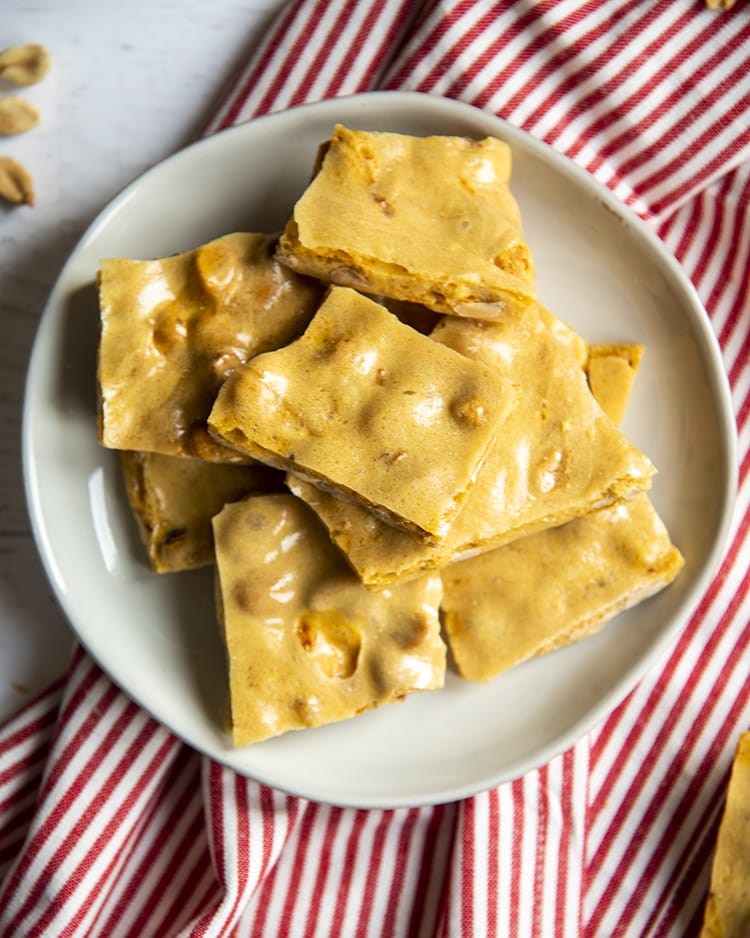 A white plate that is loaded with a pile of yellowish brown colored peanut brittle pieces.