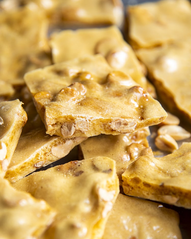 Peanut brittle piled together. The top piece shows peanuts coming through the side and top of the brittle.