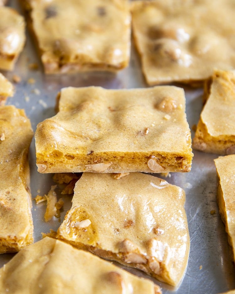 A piece of peanut brittle laying slight on top of another piece, with more surrounding it on a silver tray.