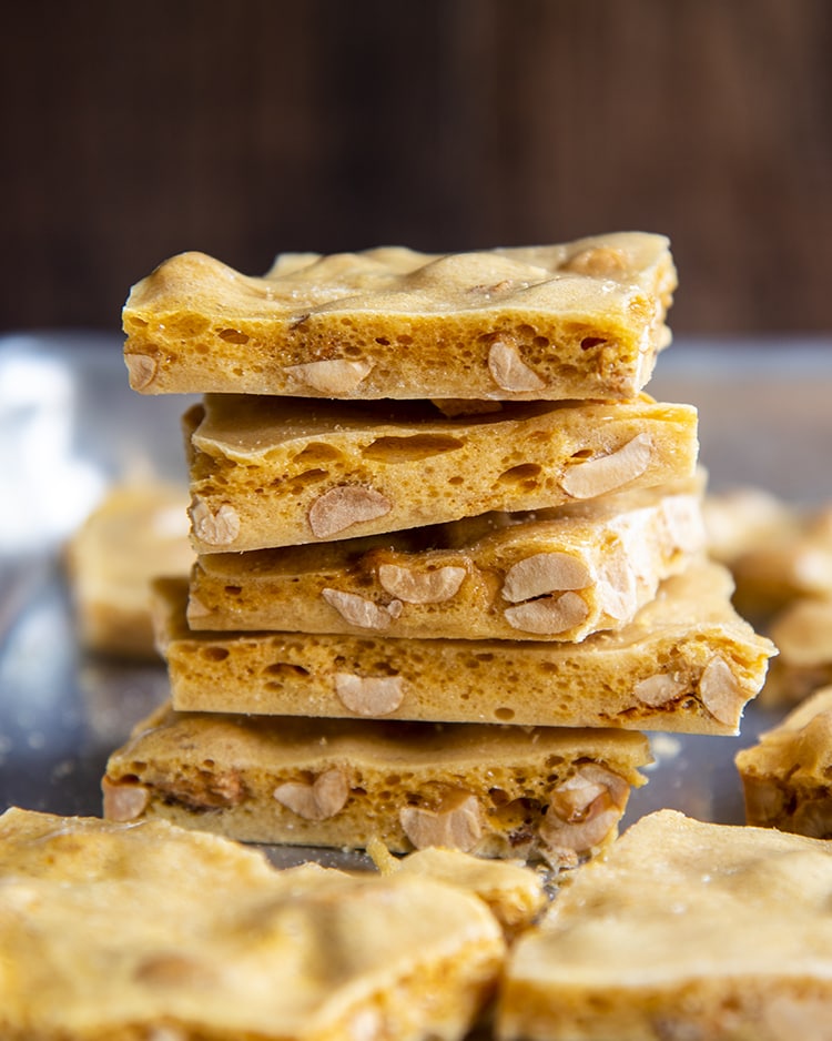 A stack of 5 pieces of peanut brittle showing the light airy layers, with bubbles in the brittle, and peanuts inside.