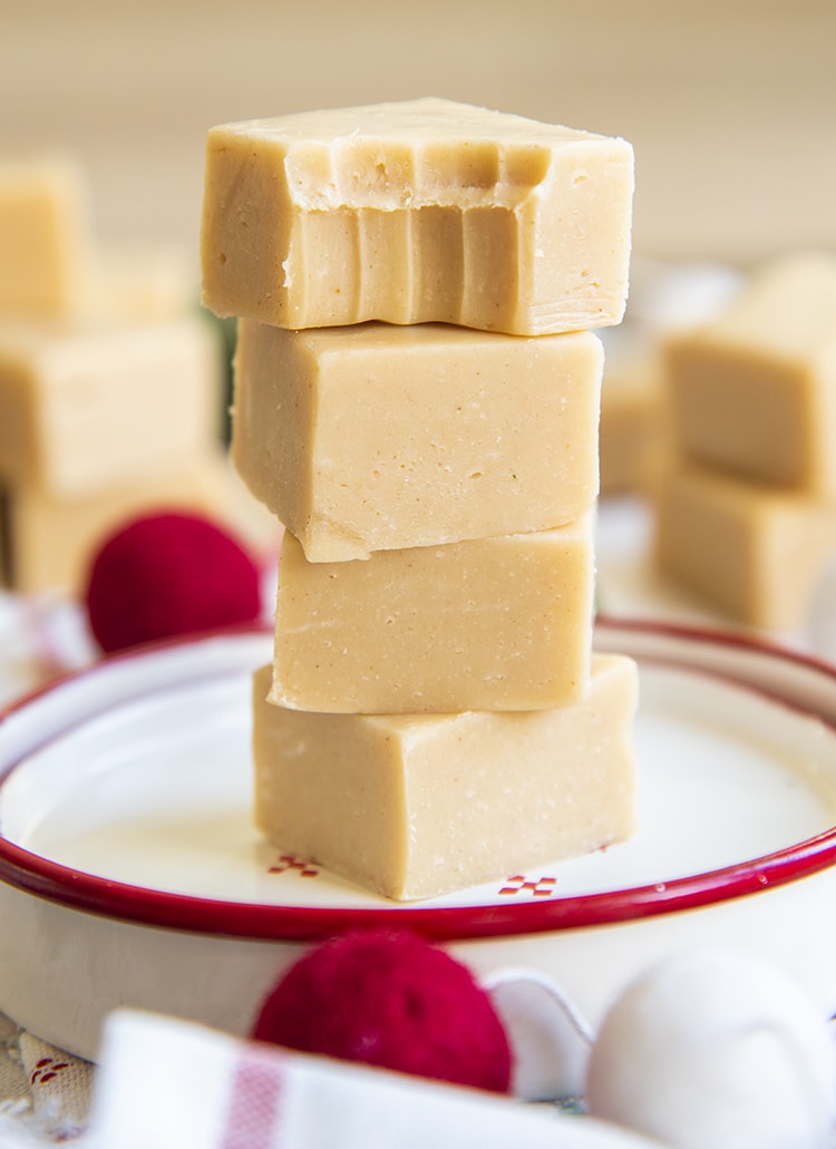 A stack of 4 pieces of peanut butter fudge on a white plate. The top piece has a bite taken out of it.