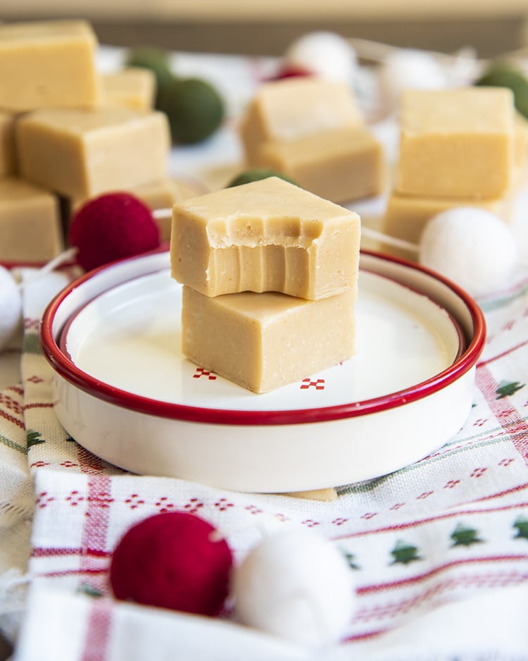 Two pieces of peanut butter fudge on a small white plate. The top piece has a bite taken out of it.