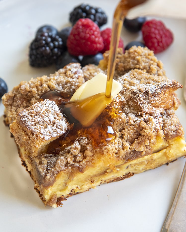 A piece of overnight french toast casserole topped with berries and syrup is being poured over the top.