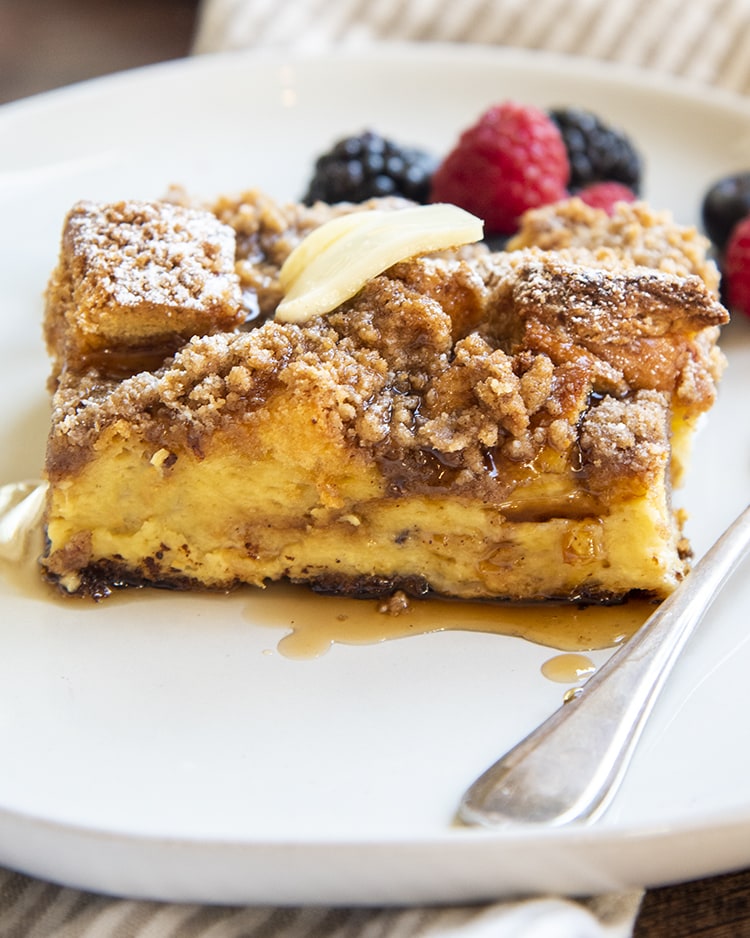 A piece of overnight french toast casserole topped with berries and syrup.