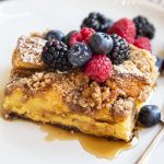 A piece of overnight french toast casserole topped with berries and syrup.