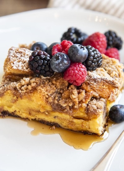 A piece of overnight french toast casserole topped with berries and syrup.