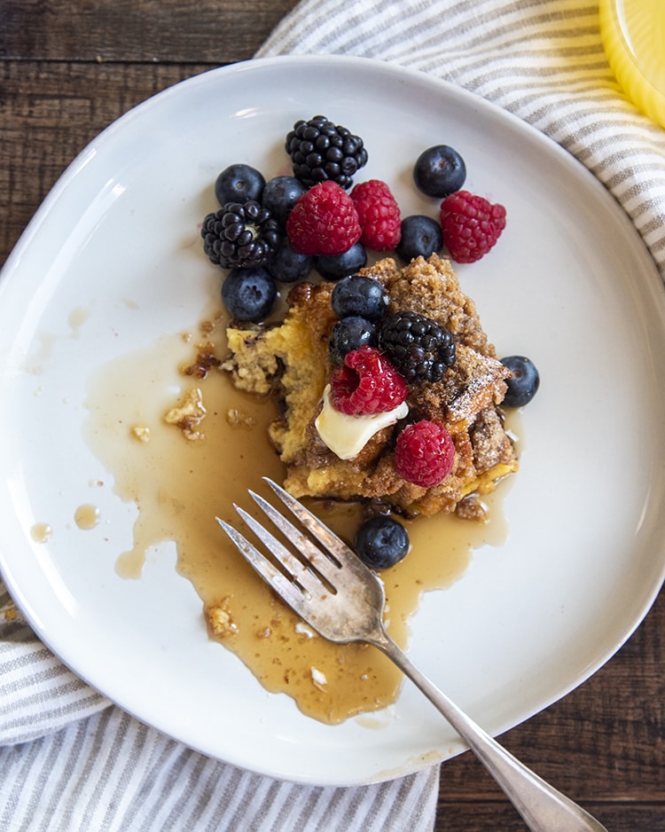 A half eaten piece of french toast casserole on a plate with a fork laying in the syrup.