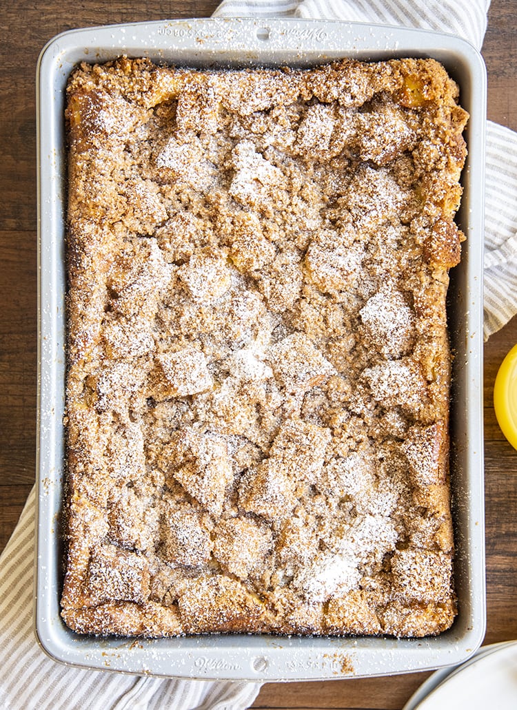 A pan of overnight french toast from above, with a crumb topping, and sprinkled with powdered sugar.