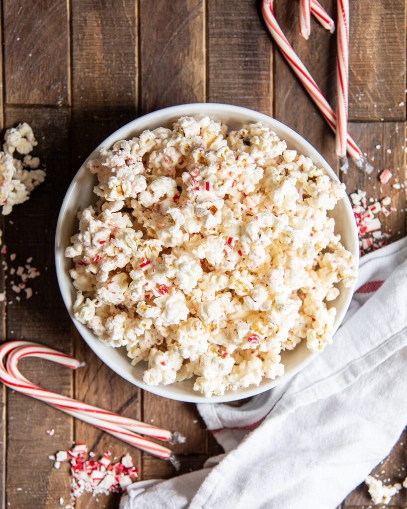 An above view of a bowl of white chocolate popcorn next to candy canes. 